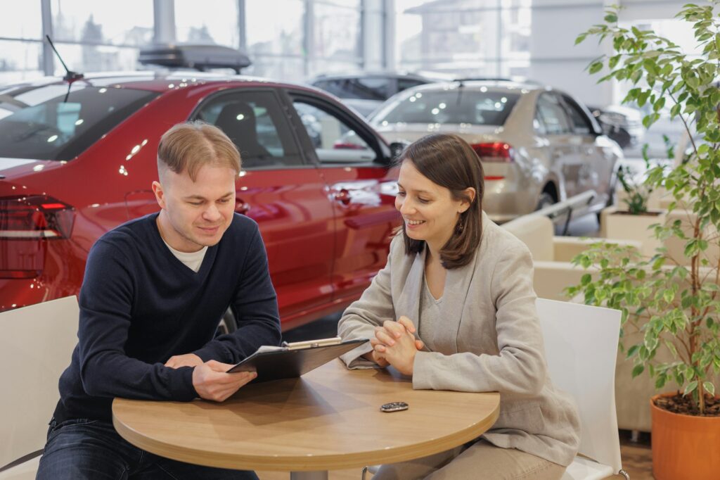 man buys a car at a car dealership. A female salesperson and car rental helps with the purchase