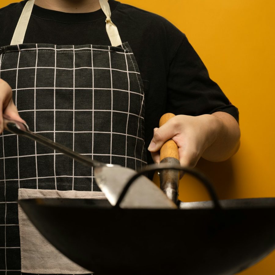 Chief wearing apron holding spatula and frying pan isolated on yellow background.